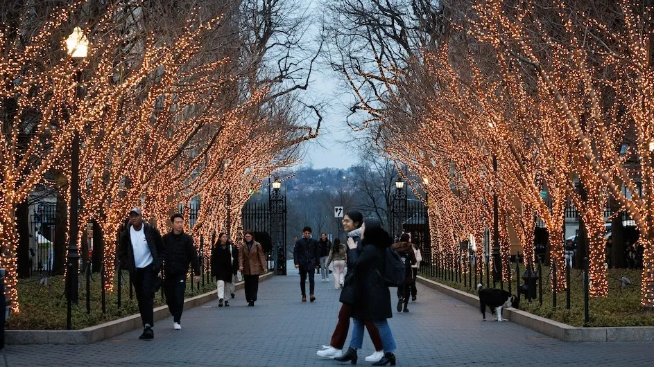 Students walking along College Walk at Columbia during the winter when the trees are lit up.