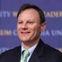 A man smiling wearing a dark suit and a green tie