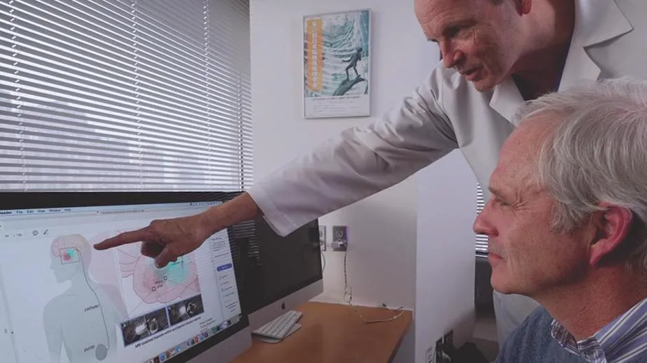 A doctor points to a computer diagram showing how a pump can deliver chemotherapy drugs to the brain.