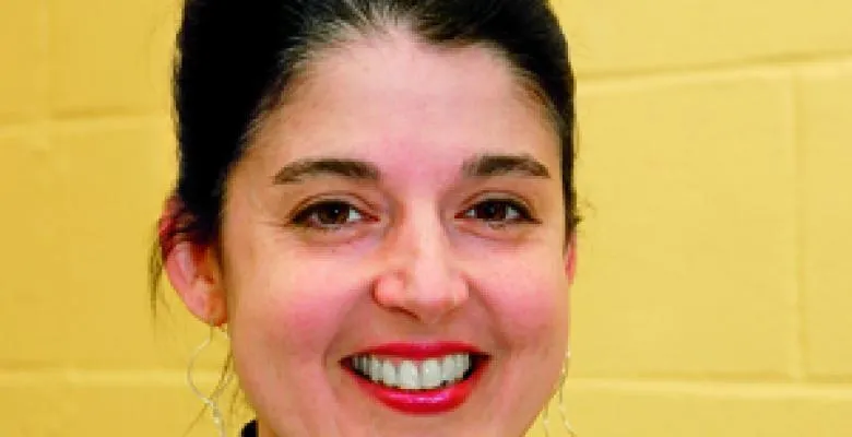 Headshot of Debora Cullen stands in front of a yellow wall with a wide smile into camera lens her hair dark and pulled away from face.