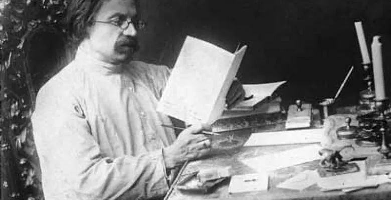 Vintage black & white image of Sholem Aleichem seated at a desk reading a book