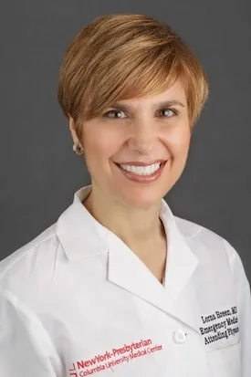 Female-presenting person with blonde hair, in lab coat, smiling. 