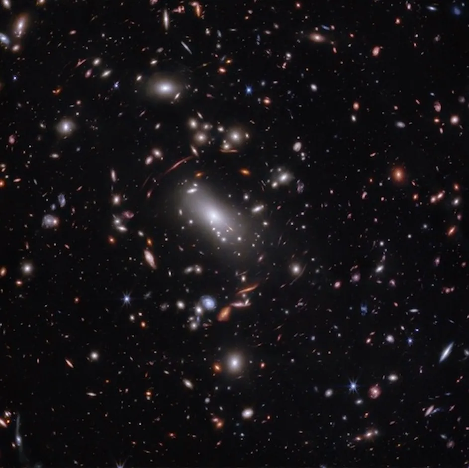 Thousands of glimmering galaxies are bound together by their own gravity, making up a massive cluster formally classified as MACS J1423 in the foreground of this image. The largest bright white oval in the center is a supergiant elliptical galaxy and the dominant member of this galaxy cluster. The galaxy cluster acts like a lens, magnifying and distorting the light of objects that lie well behind it, an effect known as gravitational lensing that has big research benefits. 