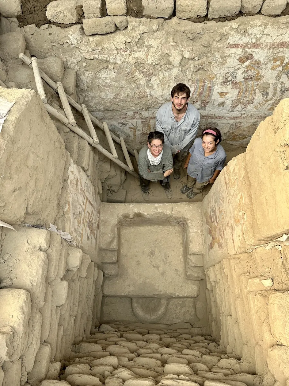 Lisa Trever stands, with research assistants Joseph Senchyshyn and Riley Tavares, behind the painted throne within the Hall of the Moche Imaginary. Photograph by José Antonio Ochatoma Cabrera