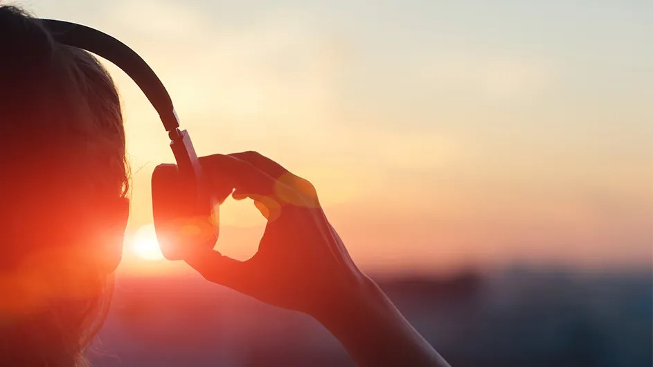 A person listens to headphones while staring into the sunset