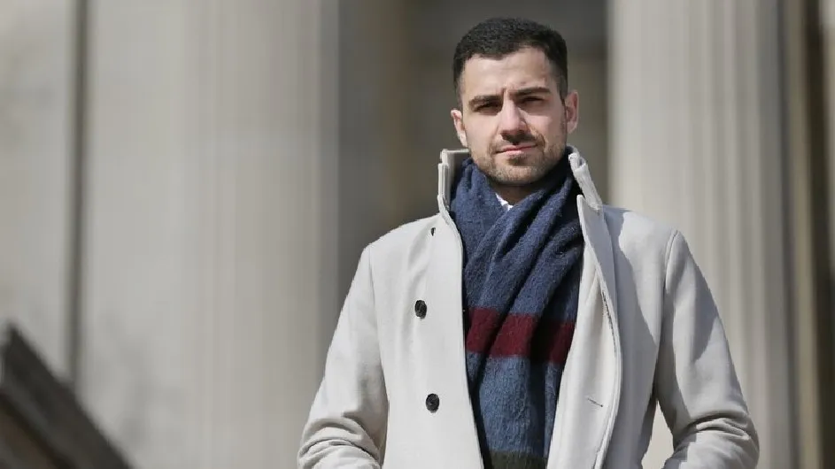 A man wearing a scarf is standing in front of columns.