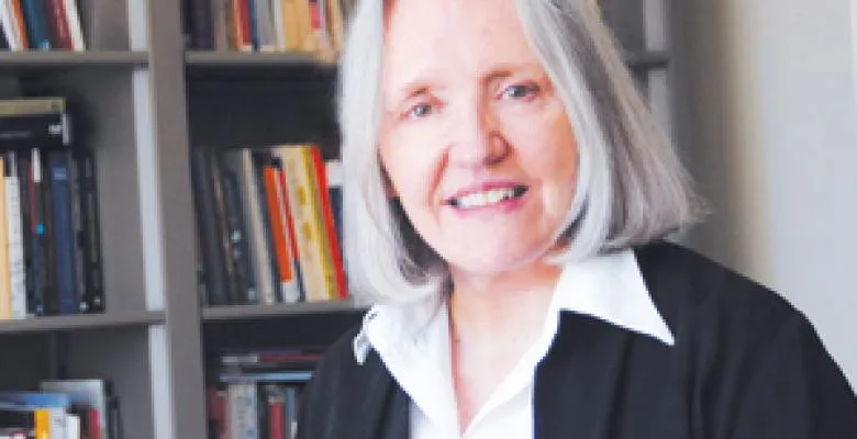 Saskia Sassen smiles while looking into camera dressed in a black blazer and white dress shirt 