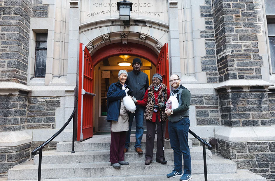 Four people holding Thanksgiving turkey donations and standing on the steps of Broadway Community Church in front of an open red door in Morningside Heights, New York City.