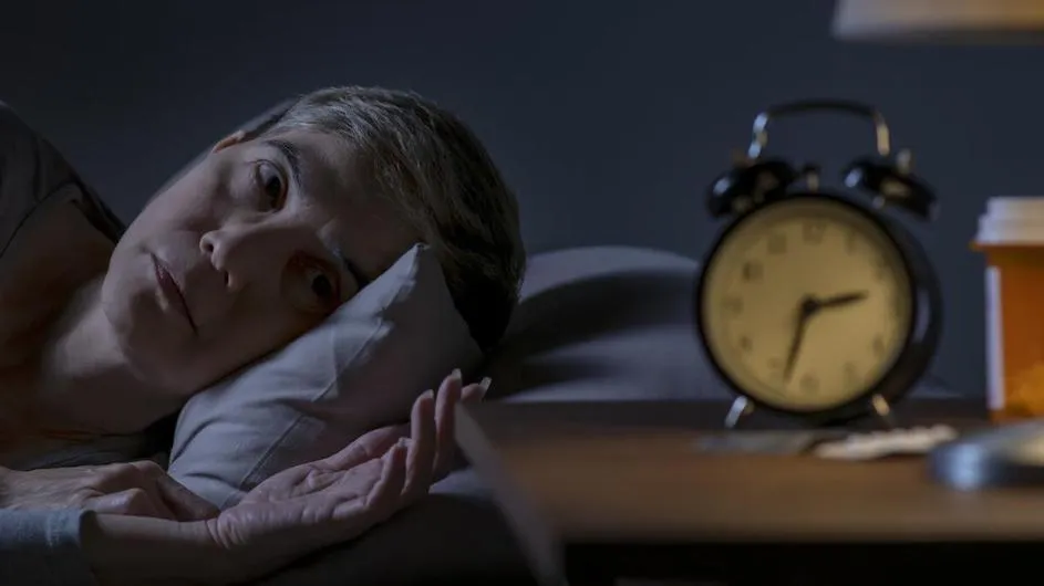 A woman lying awake at night looks at her clock.