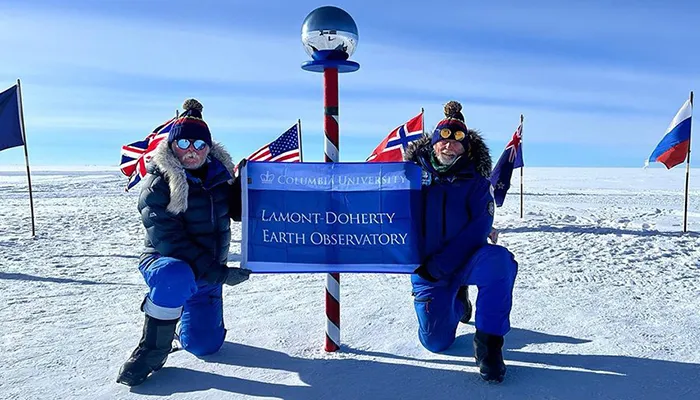 Two men pose with the south pole. 